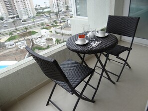 Un balcon avec deux fauteuils en osier et une table, donnant sur un parking et des immeubles.