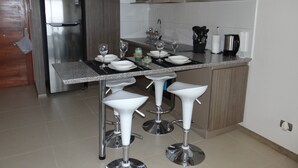 A modern kitchen with a stainless steel refrigerator, a granite countertop, and white bar stools. - Departamento Marina Horizonte 1 (Coquimbo)
