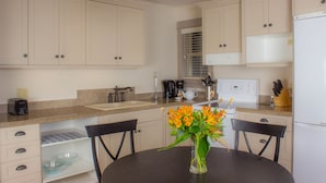 A modern kitchen with white cabinets, a granite countertop, and a dining table with chairs. - The Cottages on Salt Spring Island (Salt Spring Island)
