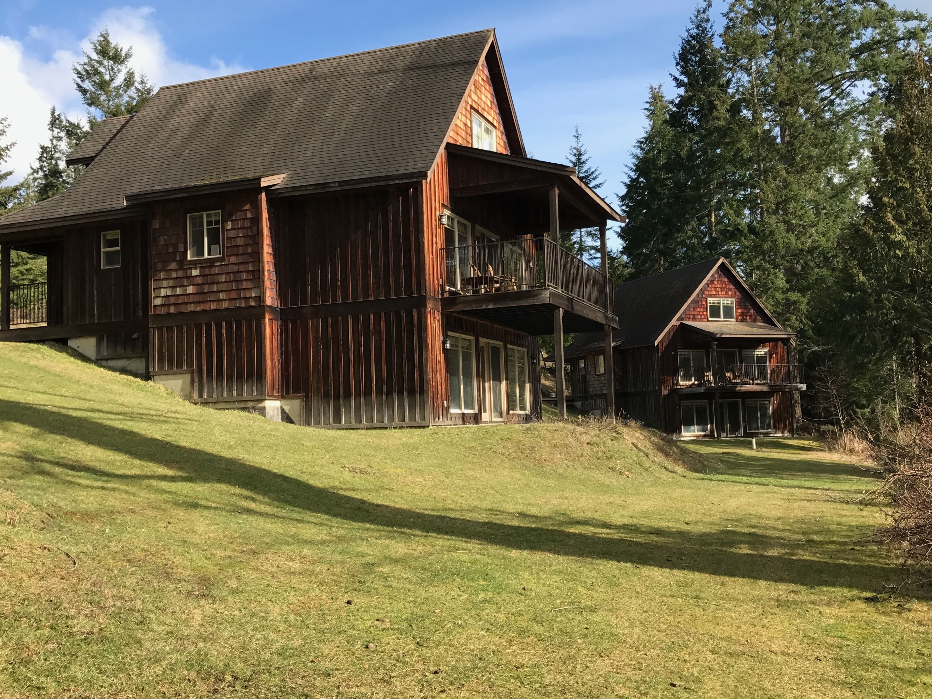 A large wooden house with a balcony and a smaller house in the background.