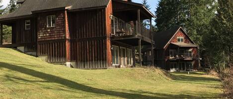 A large wooden house with a balcony and a smaller house in the background.