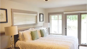 A bedroom with a large bed, a bedside table with a lamp, and a window with blinds. - The Cottages on Salt Spring Island (Salt Spring Island)