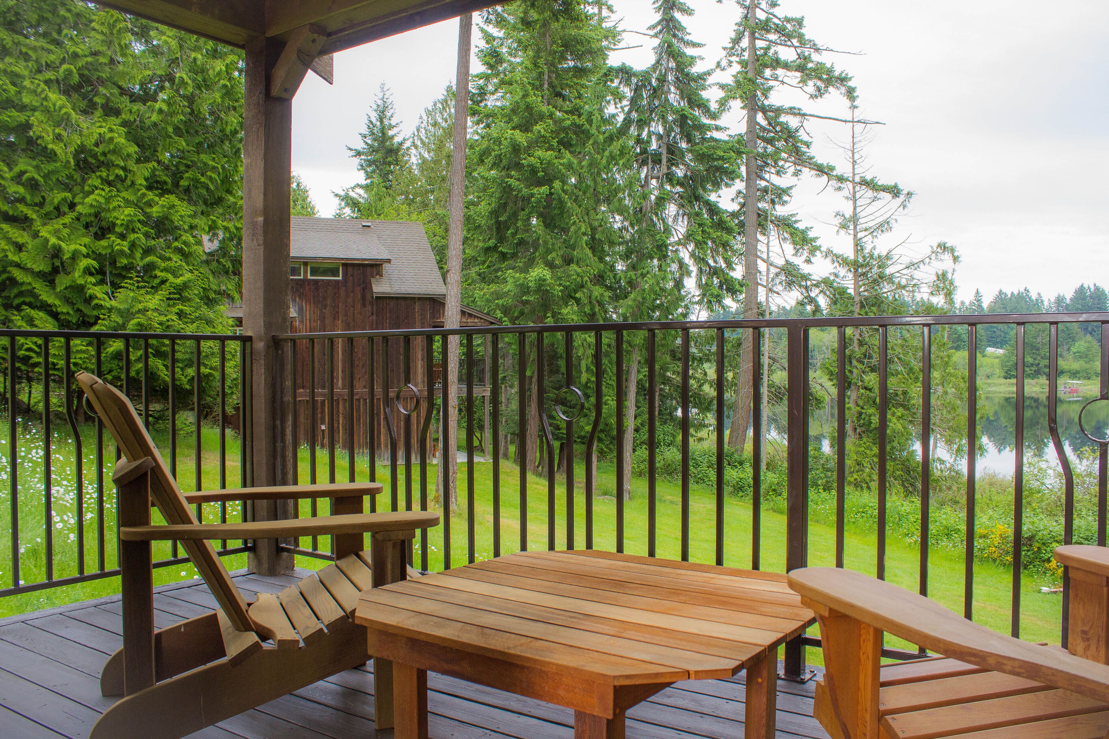 Una terraza de madera con una mesa y sillas, con vistas a un bosque y un cuerpo de agua.