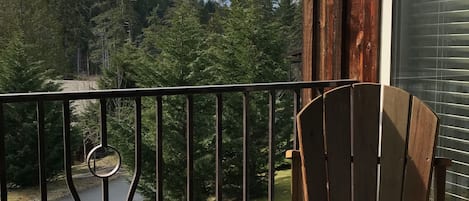 A wooden deck with a chair and a table, overlooking a river and forested area.
