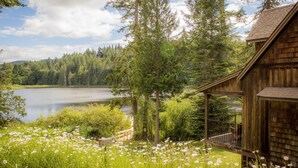 A wooden cabin with a balcony overlooking a lake surrounded by dense forest. - The Cottages on Salt Spring Island (Salt Spring Island)