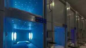 A row of hotel rooms with individual beds, each equipped with a control panel and a ceiling light fixture.