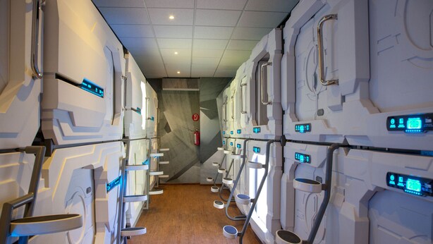 A row of modern, white, self-contained restrooms with digital displays and metal handles.