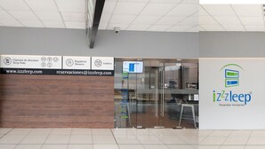 A hotel entrance with a reception desk, a glass door, and a staircase leading to an upper level.