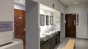 A modern bathroom with three sinks, a bench, and a towel deposit sign.