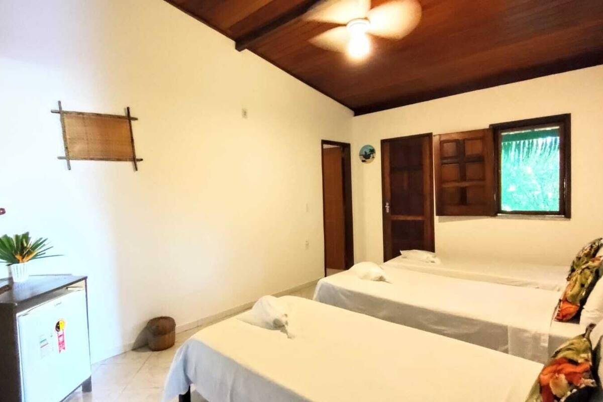 A room with two beds, a wooden ceiling, a small desk with a plant, and a window with a view.