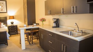 Eine kleine Hotelküche mit dunklen Holzschränken, einer Edelstahl-Spüle, einer Kaffeemaschine und einem Essbereich mit Tisch und Stühlen.