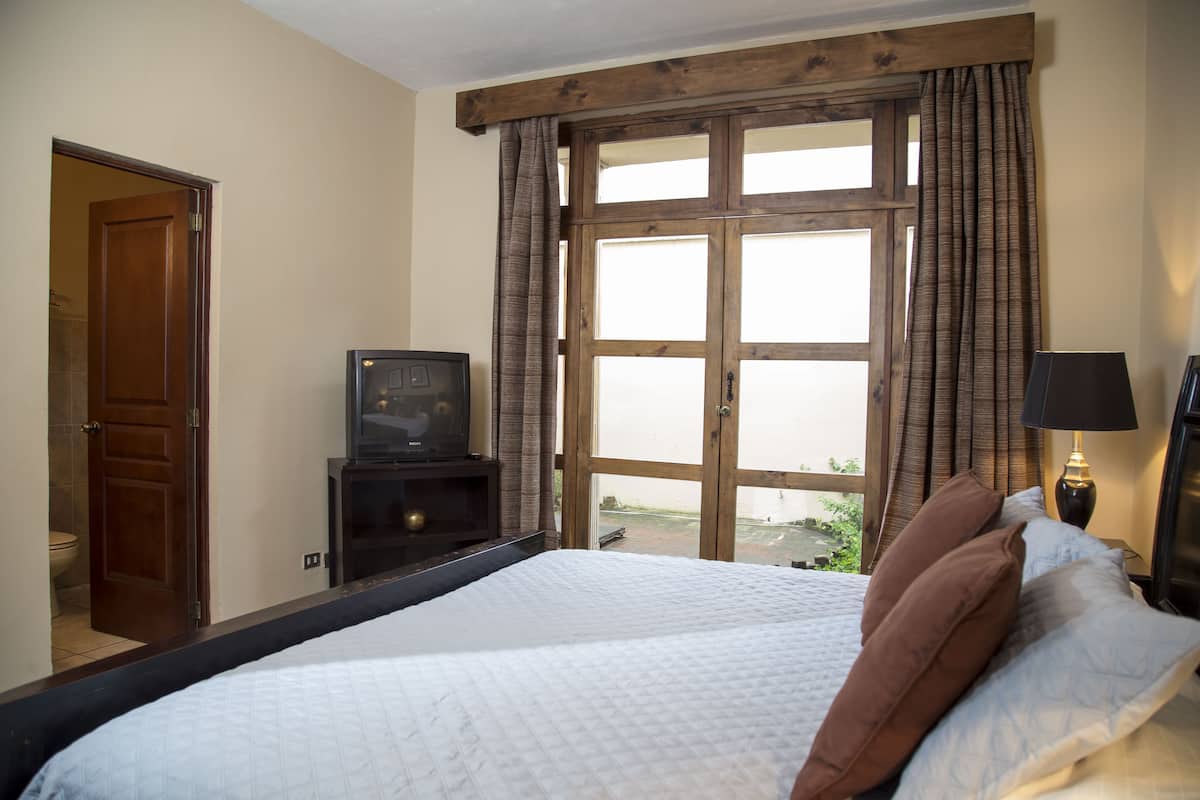 Ein Schlafzimmer mit einem großen Bett, einer Holztür, einem Fernseher auf einem Schrank und einem Fenster mit Vorhängen.