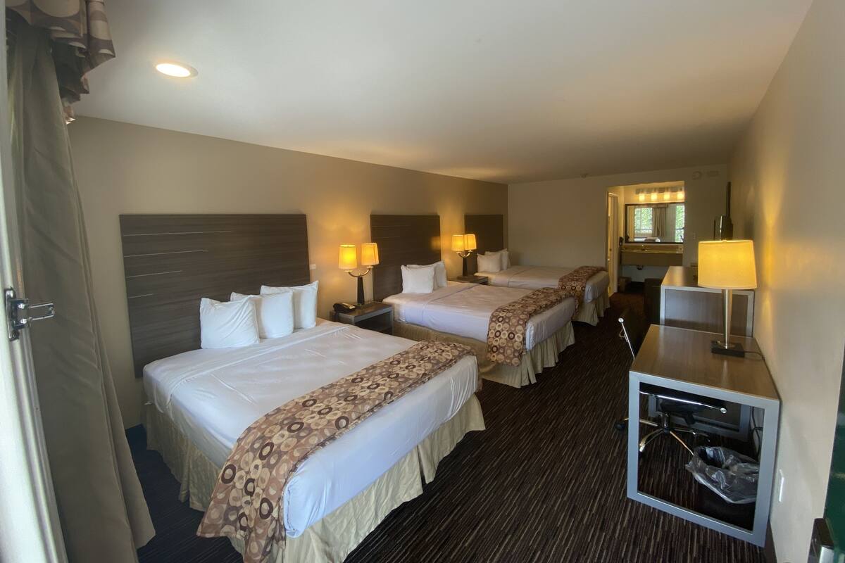 A hotel room with two beds, a desk with a lamp, a mirror, and a small TV.
