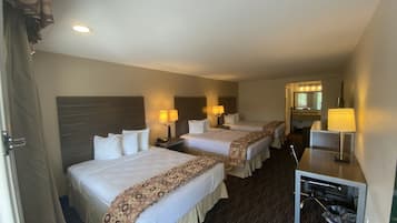 A hotel room with two beds, a desk with a lamp, a mirror, and a small TV.
