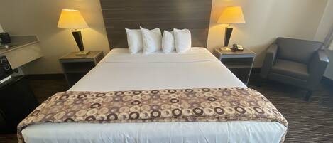 A hotel room with a large bed, two bedside tables with lamps, a chair, and a desk with a telephone.