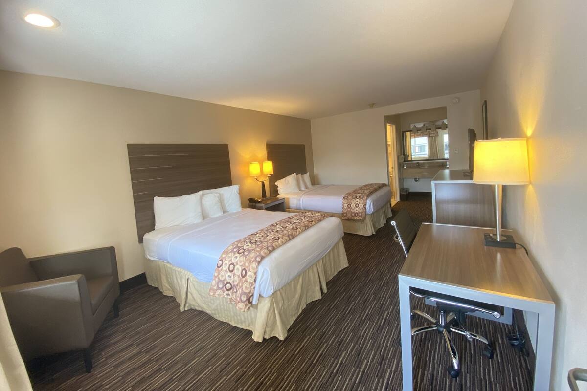 A hotel room with two beds, a desk, a chair, a mirror, and a bathroom visible through an open door.