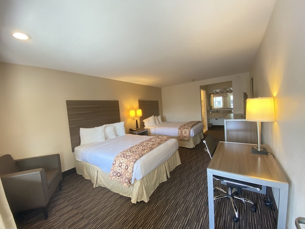 A hotel room with two beds, a desk, a chair, a mirror, and a bathroom visible through an open door.