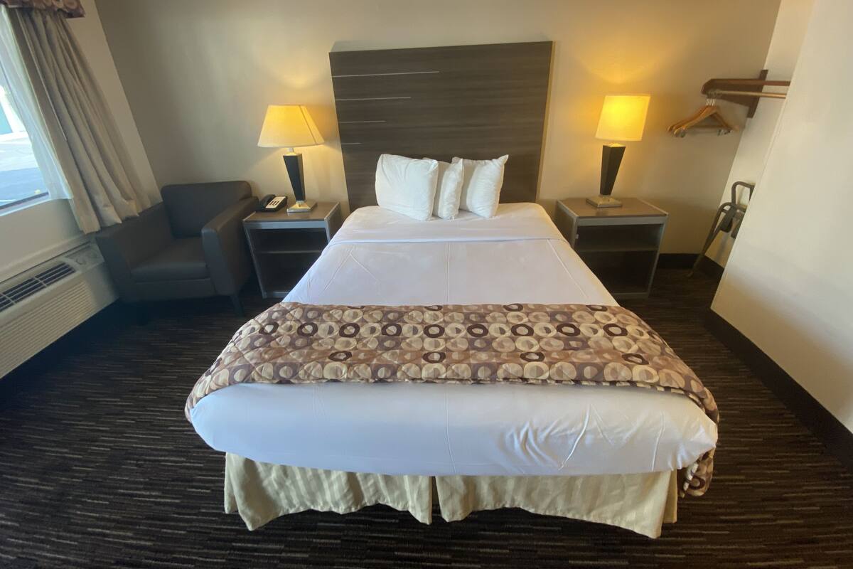 A hotel room with a large bed, two bedside tables, a chair, and a window with curtains.