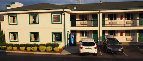 A motel with a two-story structure, a Pepsi sign, and two cars parked in front.