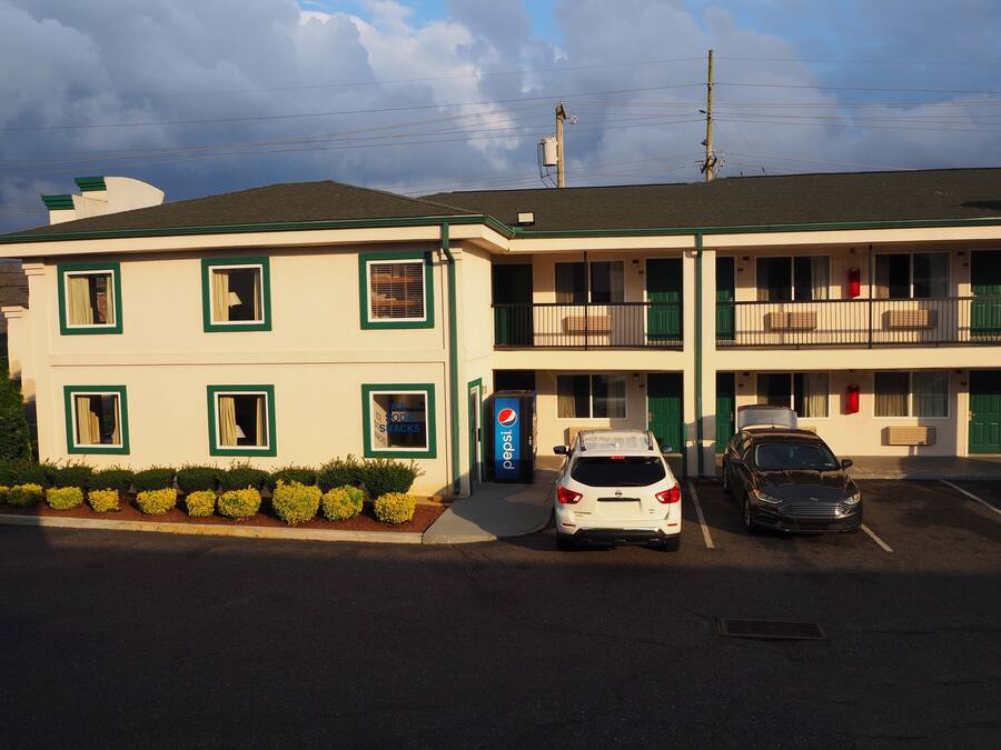 A motel with a two-story structure, a Pepsi sign, and two cars parked in front.