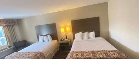 A hotel room with two beds, a nightstand with a lamp, a chair, and a window with curtains.