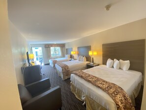 Habitación de hotel con dos camas, un escritorio y una silla. Hay lámparas en las mesitas de noche y una ventana con cortinas.