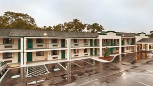 A multi-story motel with a flat roof, a parking lot, and a small landscaped area. - Garden State Inn (Absecon)