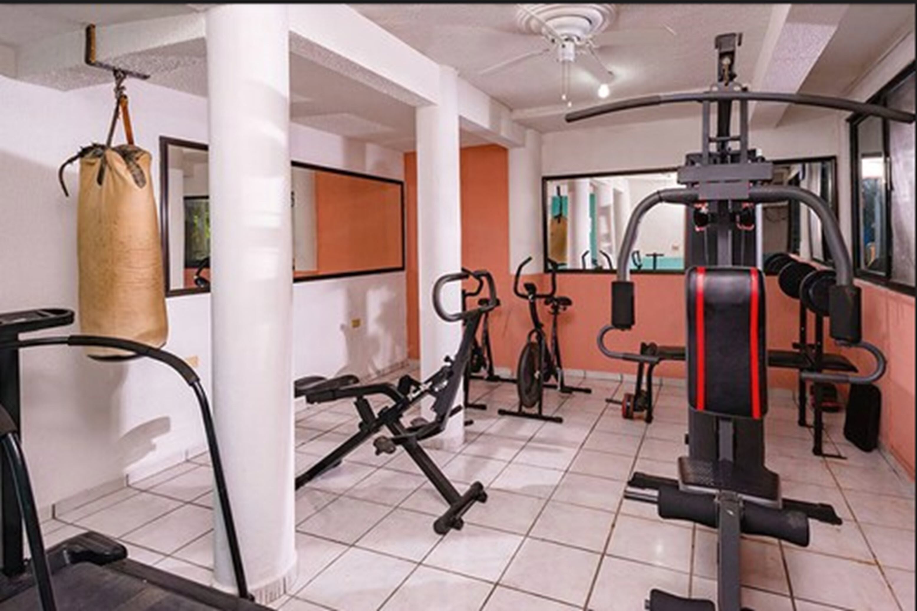 Un gimnasio con equipo de ejercicio, un saco de boxeo y un espejo.