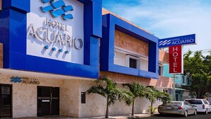 Un hôtel appelé « Hotel Aquario », doté d’une façade bleue moderne, de palmiers à l’avant et surplombant un ciel d’un bleu limpide.