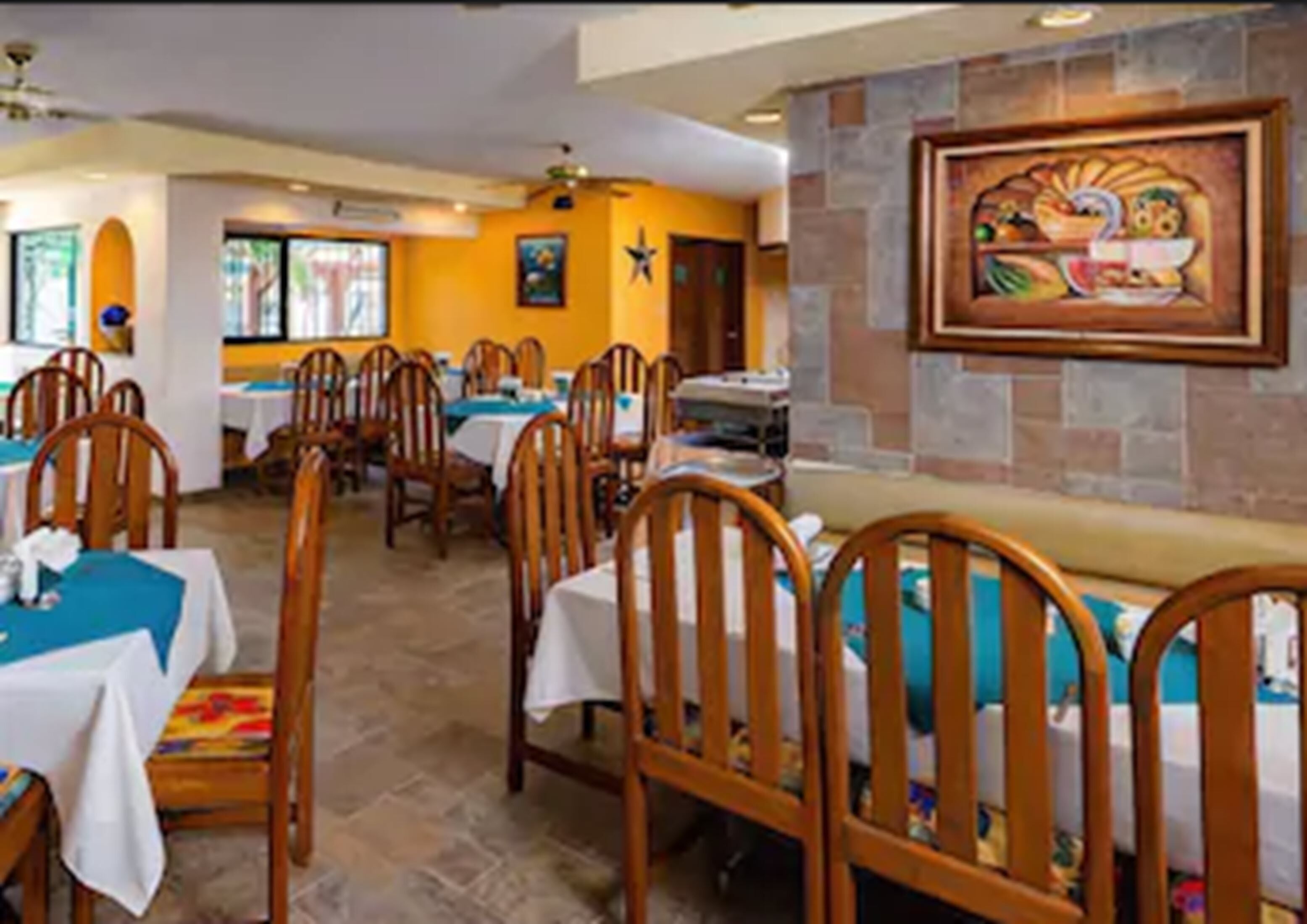 A dining area with wooden chairs and tables, a stone wall with a painting, and a star decoration on the wall.
