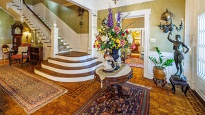 A grand staircase leading to a second floor, a large floral arrangement on a table, and a statue on a pedestal. - Belle Oaks Inn (Gonzales)