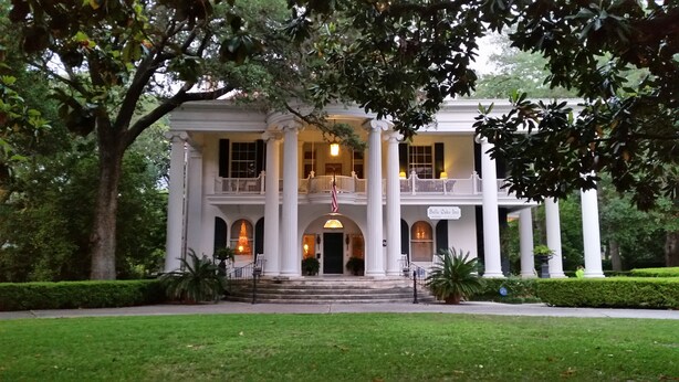 A large, two-story building with a central entrance flanked by columns, a balcony on the upper floor, and a sign reading "Belle Oaks Inn". - Belle Oaks Inn (Gonzales)