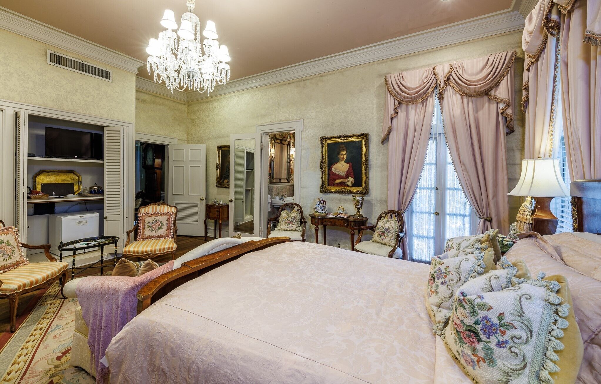 A spacious bedroom with a large bed, a chandelier, and classic decor.