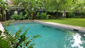 A rectangular swimming pool with clear water, surrounded by lush greenery and a well-maintained lawn. - Belle Oaks Inn (Gonzales)