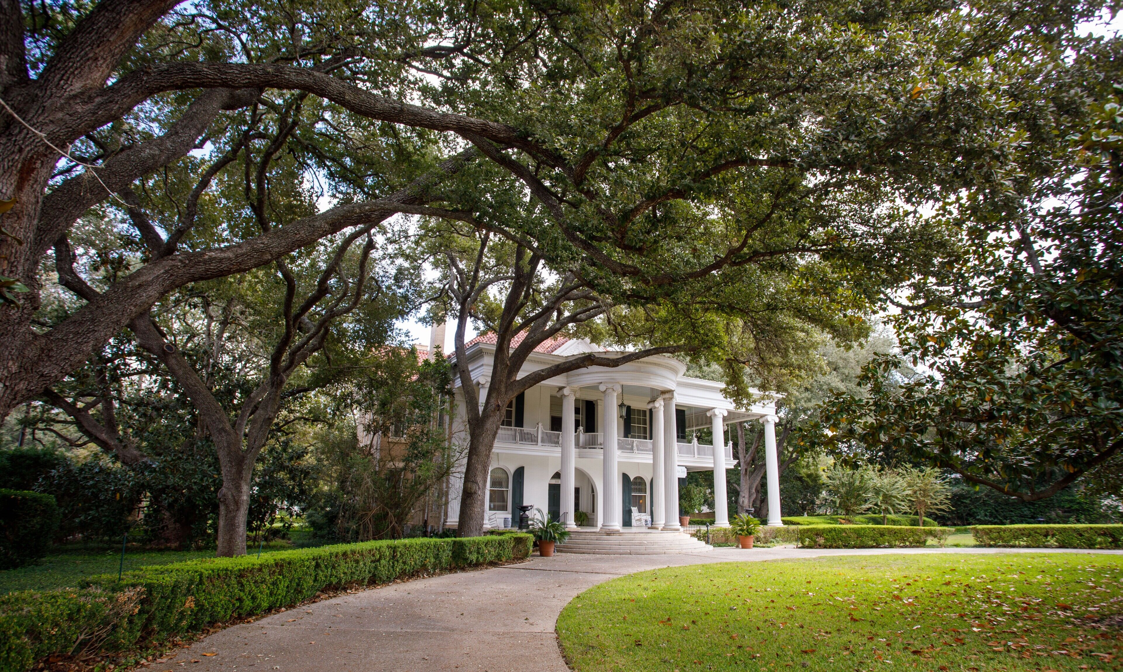 A white colonial-style building with a covered porch, surrounded by mature trees and well-maintained lawns.