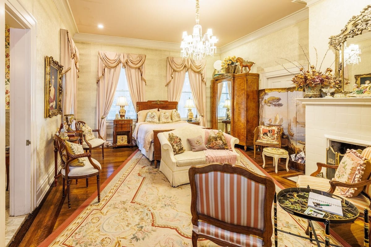 A classic, elegantly furnished room with a large bed, multiple seating areas, and a fireplace.