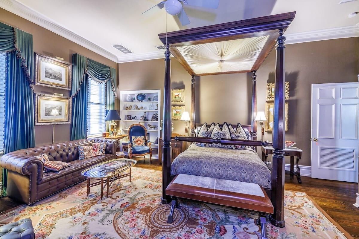 A four-poster canopy bed with a matching bench, a leather sofa, and a small table with a lamp.