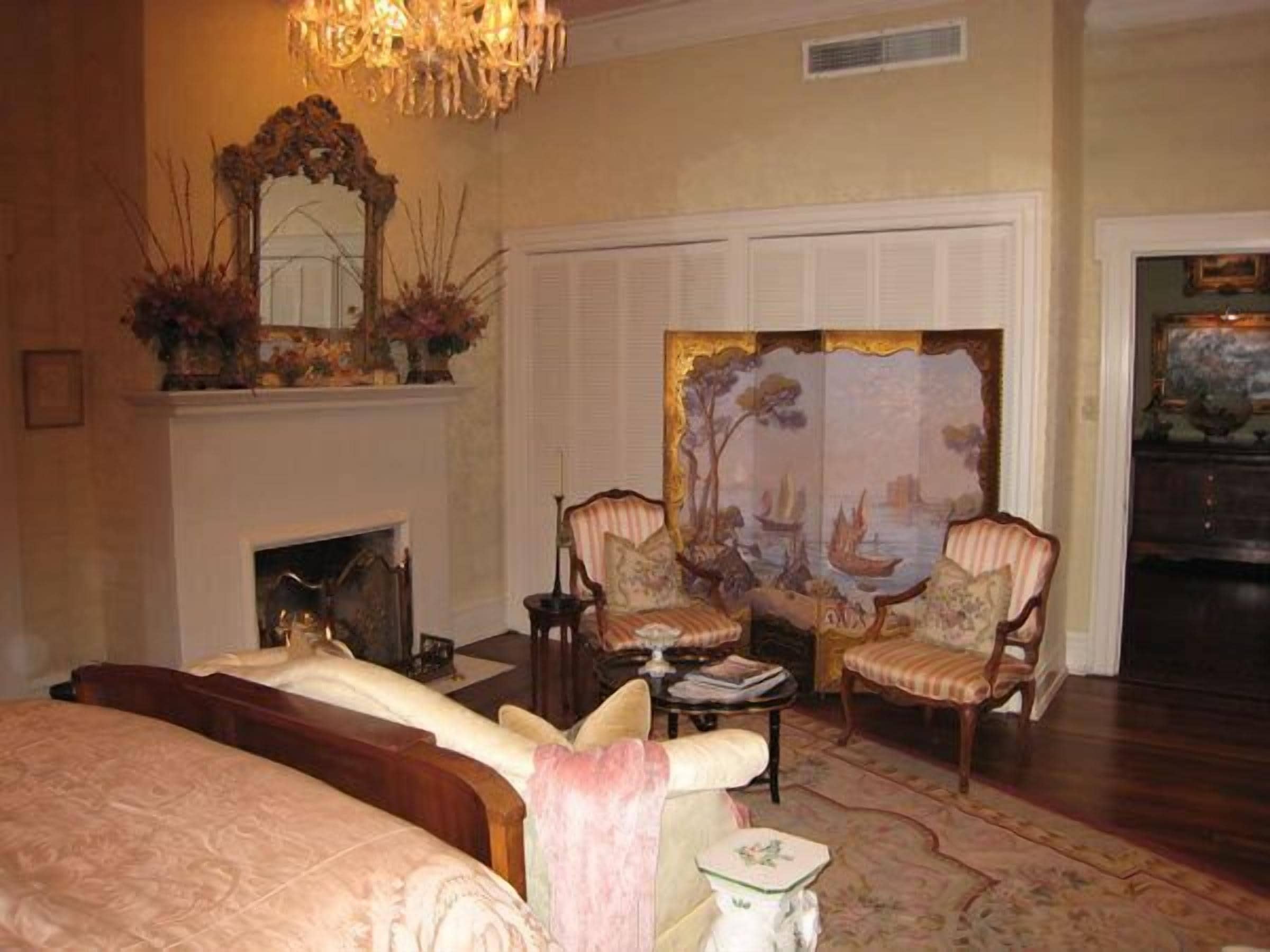 Une pièce avec une cheminée, deux fauteuils rembourrés, un canapé, une table et un grand tableau accroché au mur.