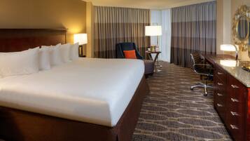 A hotel room with a large bed, a desk with a chair, a small table with a lamp, and a large mirror on the wall.