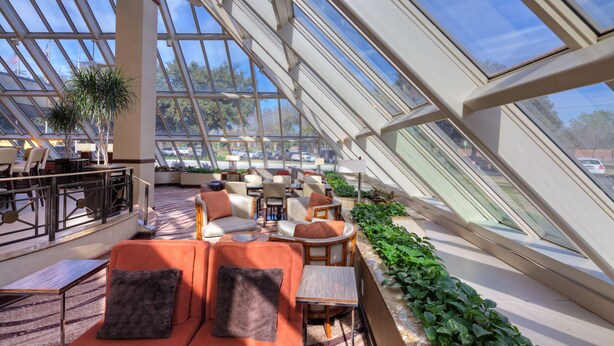 A spacious indoor area with a high ceiling and large windows, featuring seating arrangements and a view of the outdoors. - Hilton Houston Westchase (Houston)