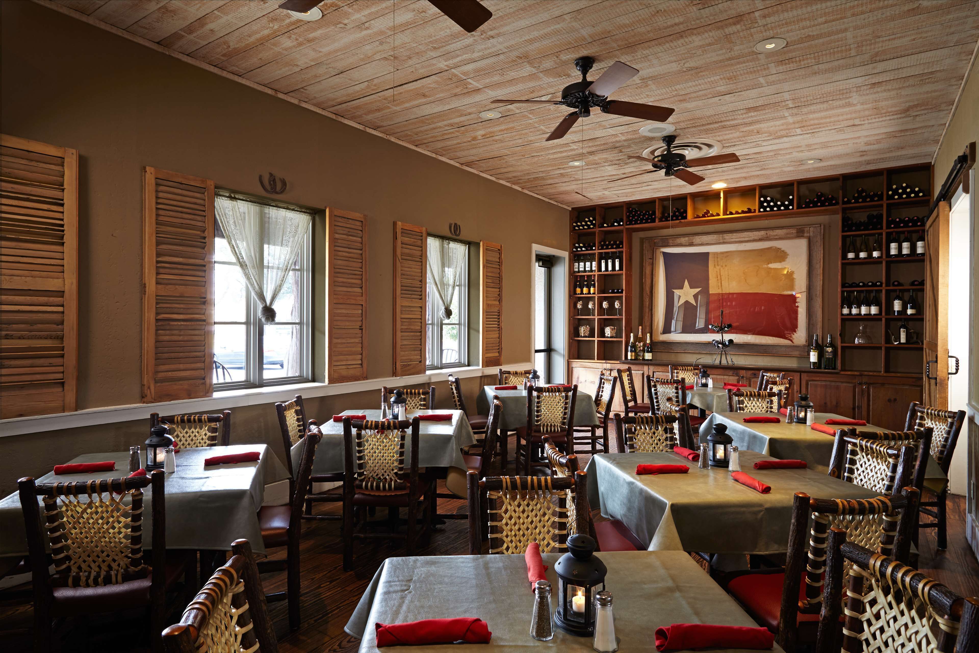 A restaurant with wooden ceiling, tables with red napkins, and a wine rack.