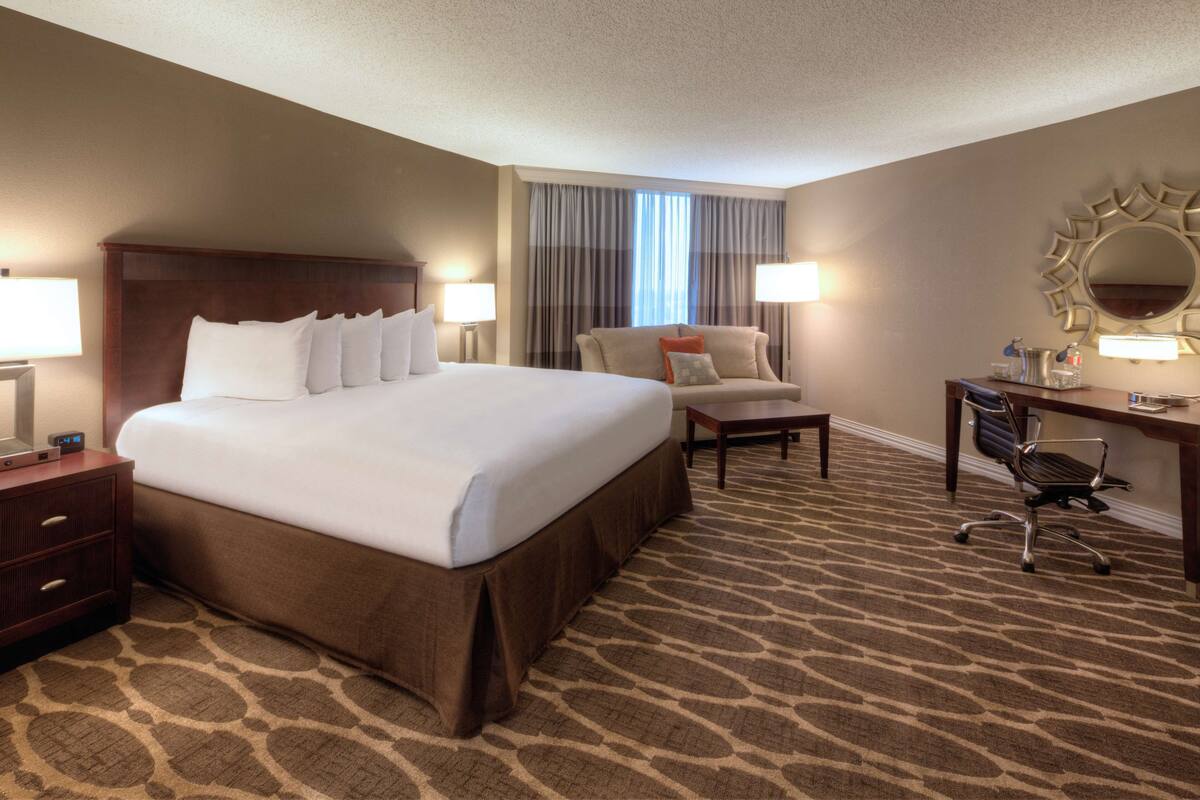 A hotel room with a large bed, a desk, a chair, and a nightstand.