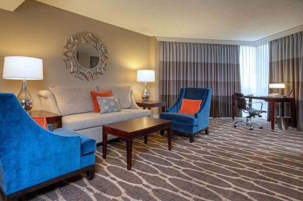 A hotel room with a sofa, armchairs, a desk, and a large window with curtains. - Hilton Houston Westchase (Houston)