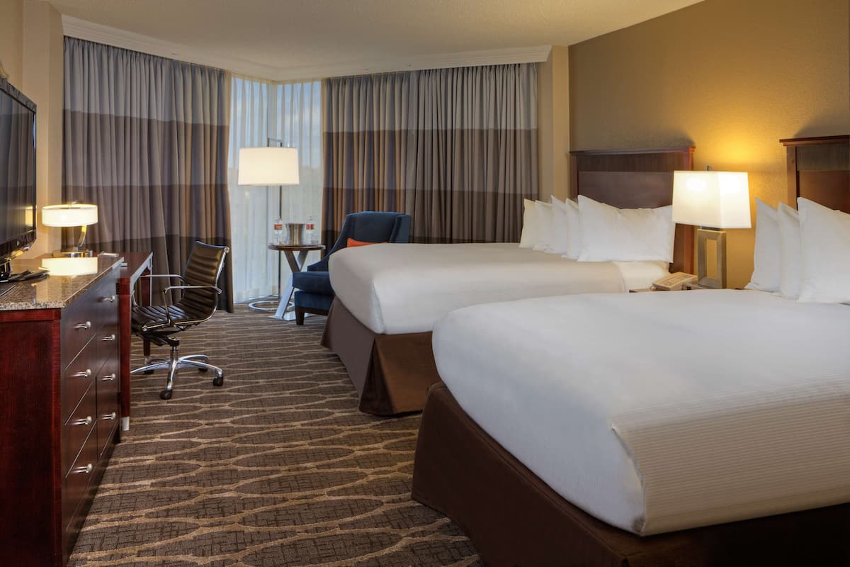 A hotel room with two beds, a desk, a chair, a TV, and a minibar.