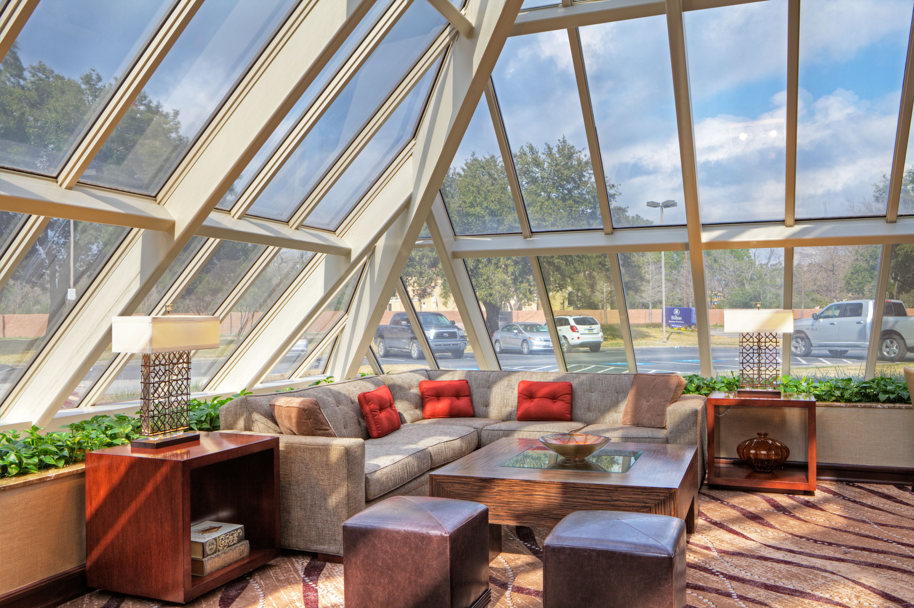 A modern interior with a glass ceiling, a sectional sofa, a coffee table, and a side table with a lamp.