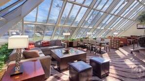 A spacious, well-lit room with a high ceiling and large windows, featuring comfortable seating, a dining area, and a view of the outdoors. - Hilton Houston Westchase (Houston)