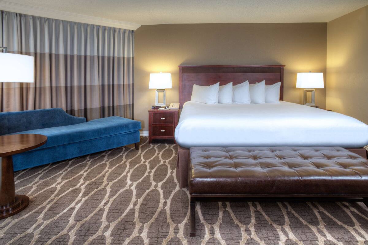 A hotel room with a large bed, a blue sofa, a wooden nightstand, and a patterned carpet.