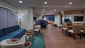 A modern hotel lobby with a blue sofa, dining area, and kitchen in the background. - TownePlace Suites by Marriott Tacoma Lakewood (Lakewood)
