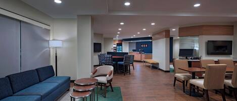 Una moderna hall d'hotel con un divano blu, zona pranzo e cucina sullo sfondo.