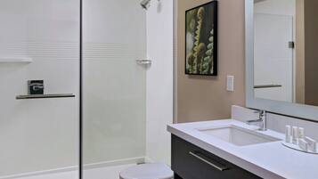 Une salle de bain moderne avec une douche à parois de verre, des toilettes blanches, un meuble-lavabo doté d’un grand miroir et un plancher en bois.